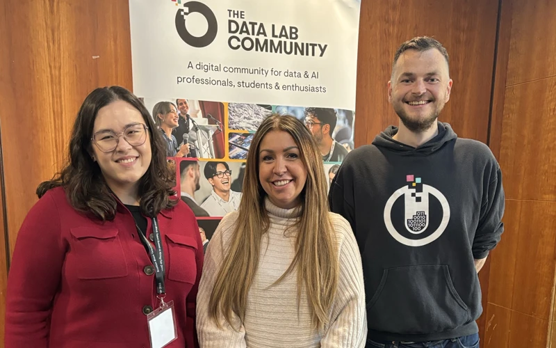 Three smiling people in front of a pop-up banner promoting The Data Lab