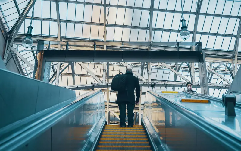 View up an escalator with a person standing at the top against the background of a glass roof.