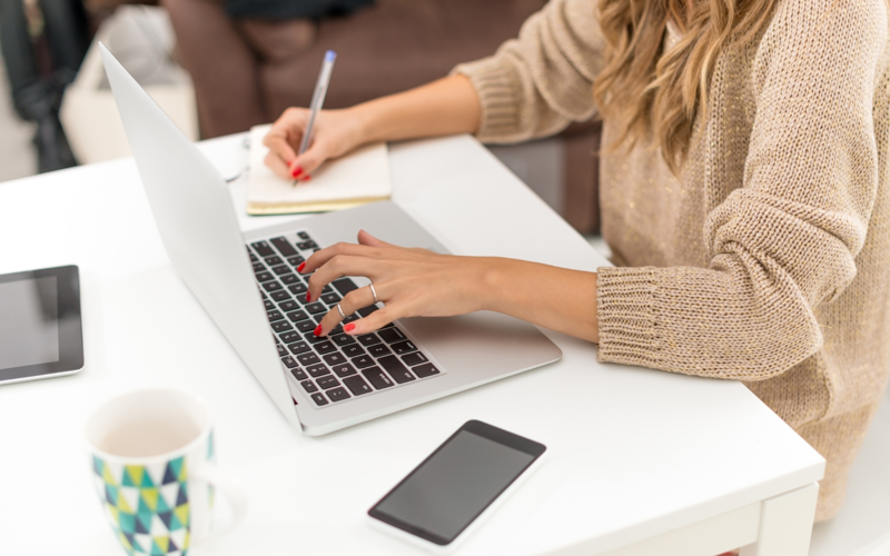Woman using laptop and writing in a notepad.