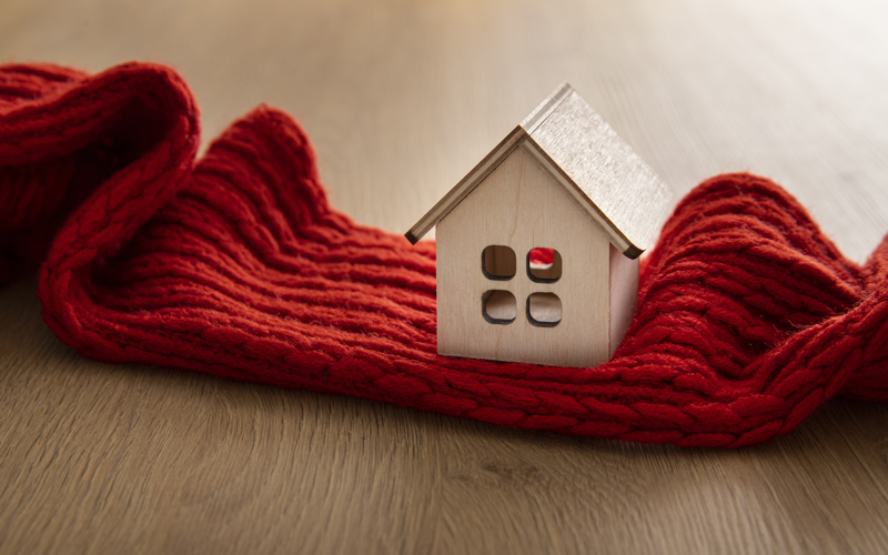 A small wooden toy house rests on a red wool scarf