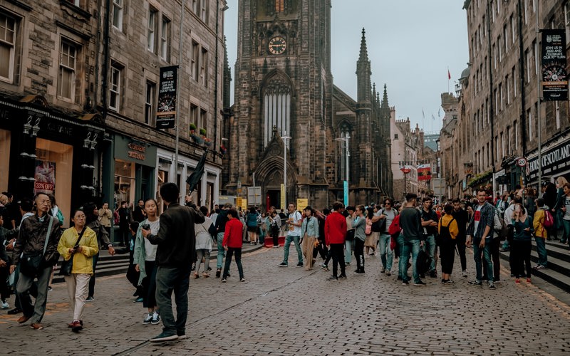 A crowd of people stand on a cobbled Edinburgh street