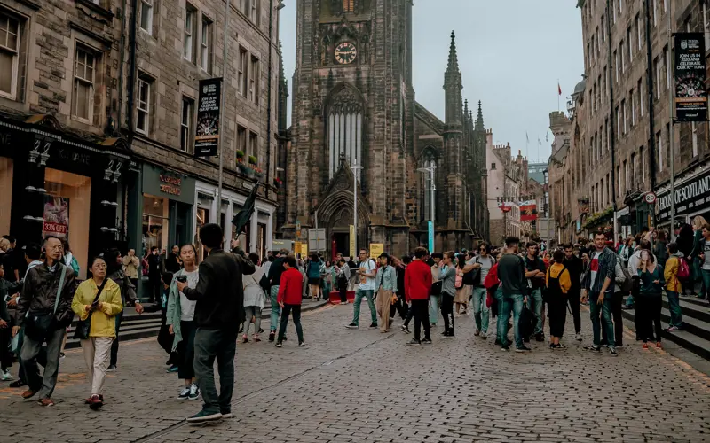 A crowd of people stand on a cobbled Edinburgh street
