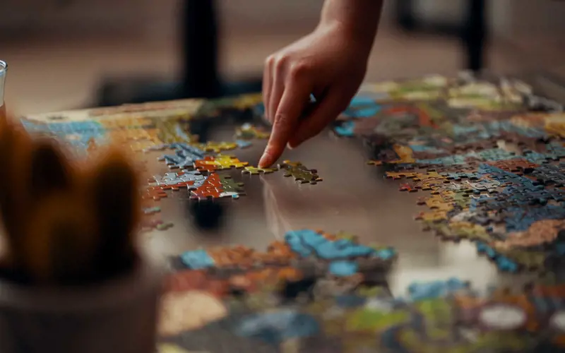 Hand placing a piece in a nearly-complete jigsaw puzzle.