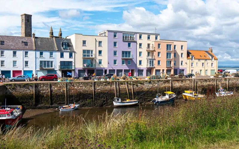 Various small boats moored in a stone harbour in front of a colourful row of buildings.