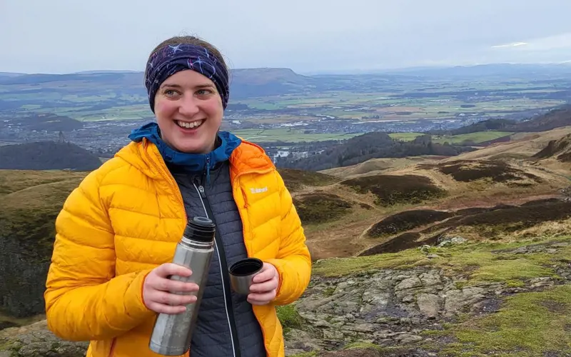 Rosie Seaman stands on top of a hill, holding a flask and smiling