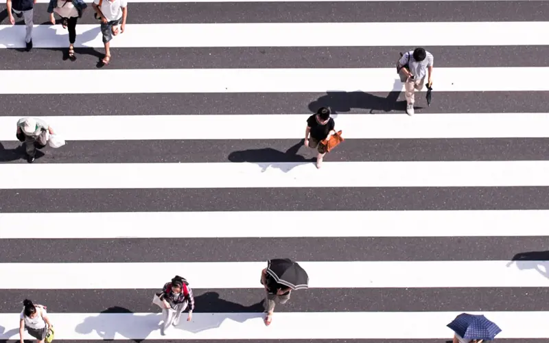 A zebra crossing in the sun with people crossing viewed from above