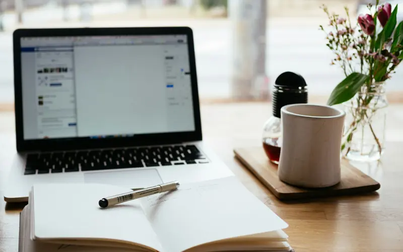 An open notebook with laptop and mug in the background