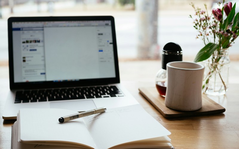 An open notebook with laptop and mug in the background