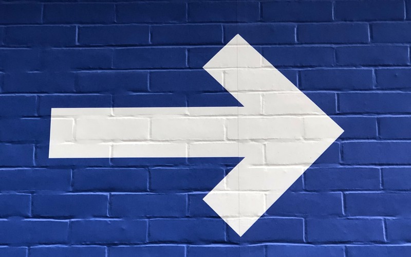 A large white arrow pointing right on a blue brick wall