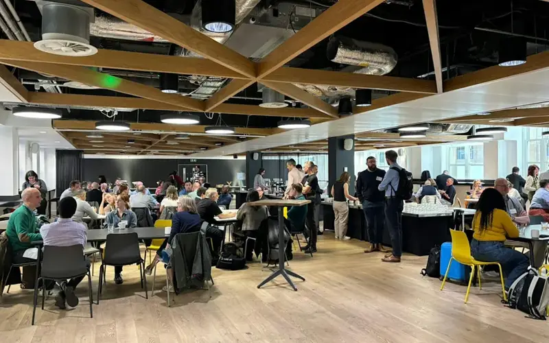 Image of a large room with people sitting at different table groupings in a workshop style setting.
