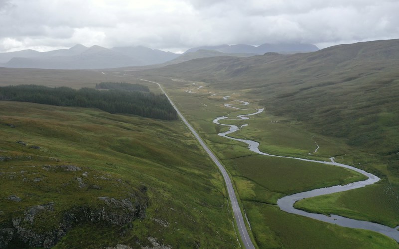 A winding river and straight road in a mountainous green valley