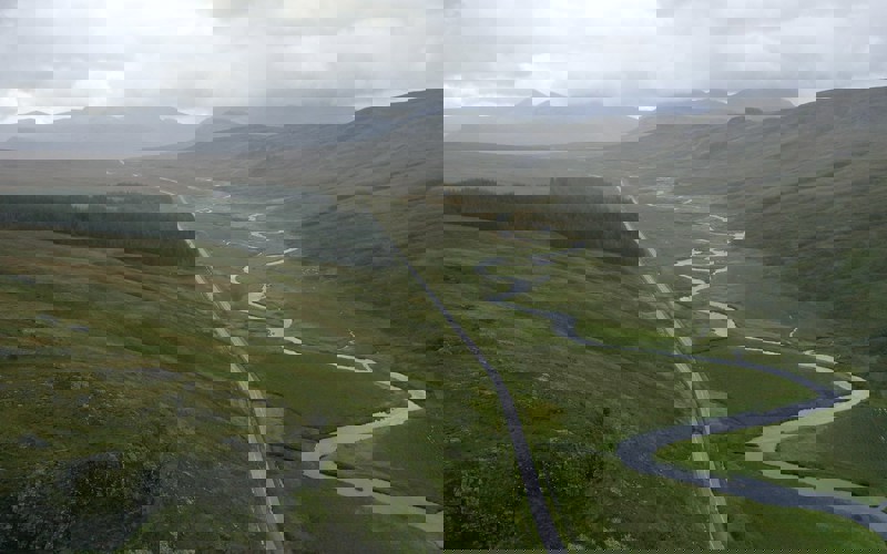 A winding river and straight road in a mountainous green valley