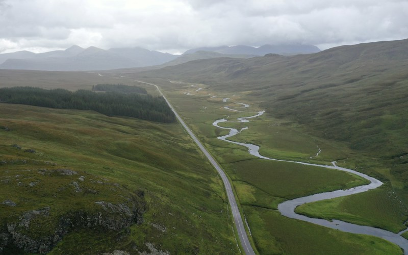 A winding river and straight road in a mountainous green valley