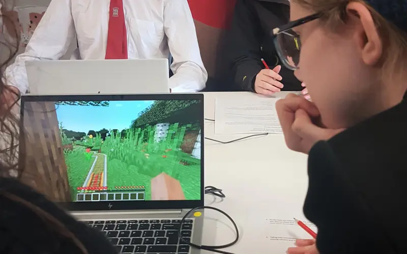 A schoolchild looking at a laptop with Minecraft on the screen