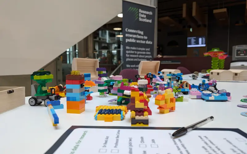 Lego models and a form sit on a desk, with an RDS banner in the background