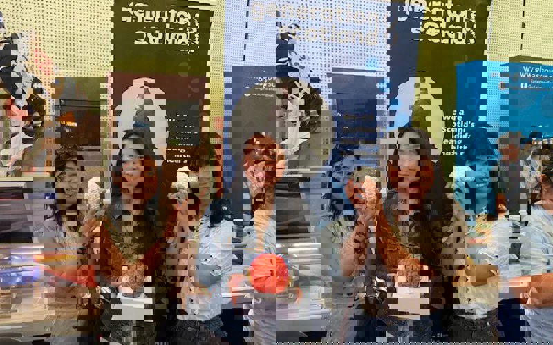 Three people hold models of brains. They are standing in front of a banner that reads