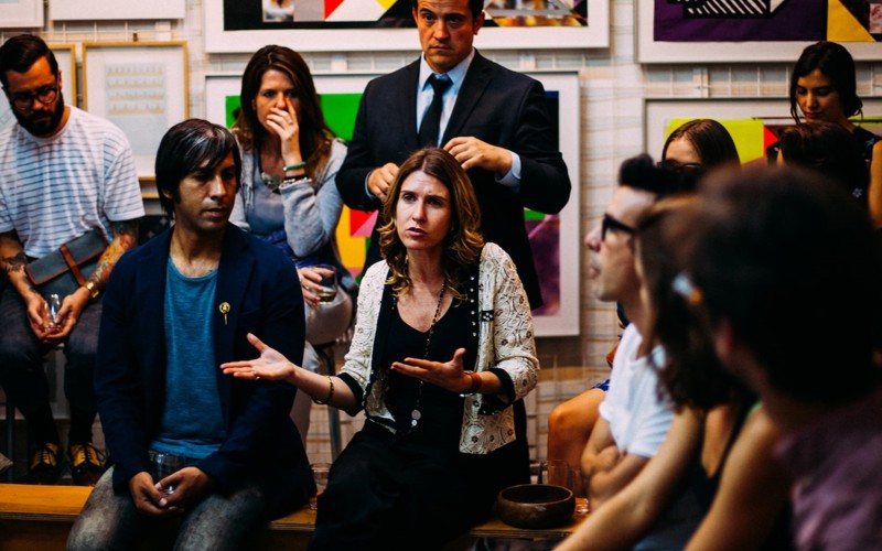 A woman talking at a public meeting surrounded by different people all seated