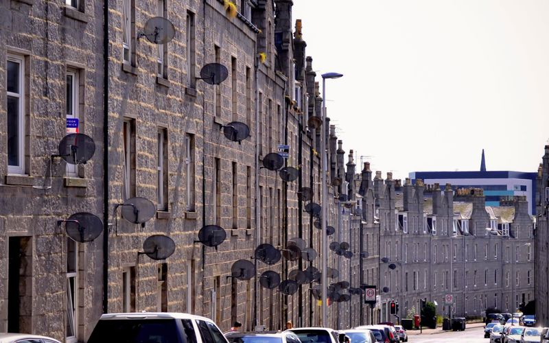 A row of tenement buildings in Aberdeen with satellite dishes on the outside.