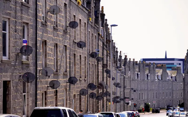 A row of tenement buildings in Aberdeen with satellite dishes on the outside.