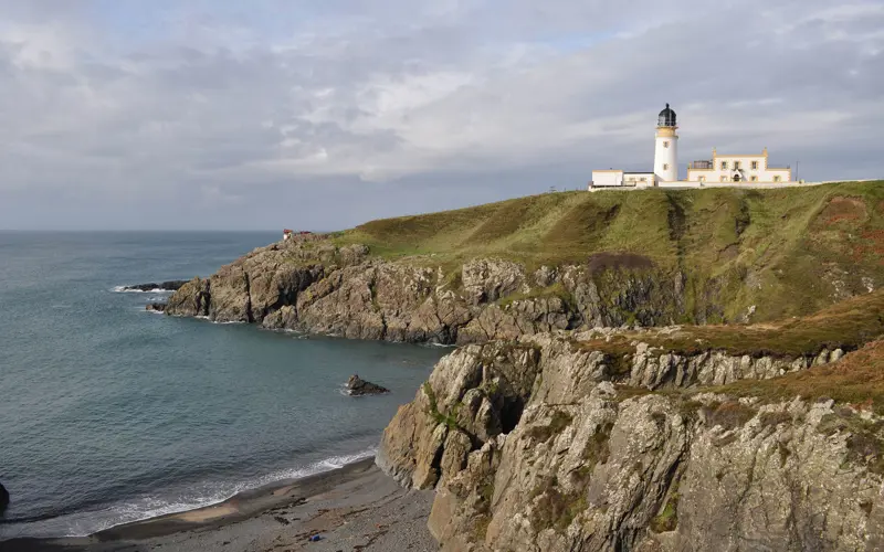 A white lighthouse at the top of sea cliffs.