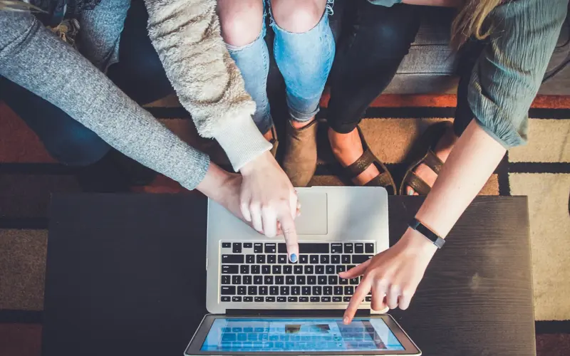 Three people viewed from above all poiting at an open laptop screen