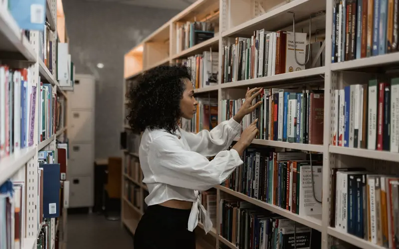 A woman choosing a book from a full library shelf.